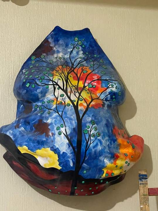 Escultura de barriga en yeso pintada con un árbol y un cielo azul.