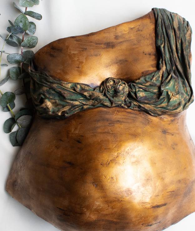 Escultura de barriga en yeso con acabado dorado y una tela pintada sobre el pecho.